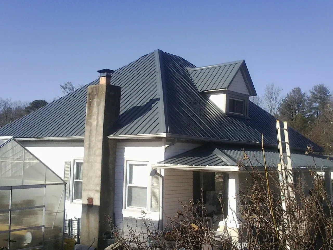Dark blue standing seam metal roof on a white farmhouse with dormer in Monrovia