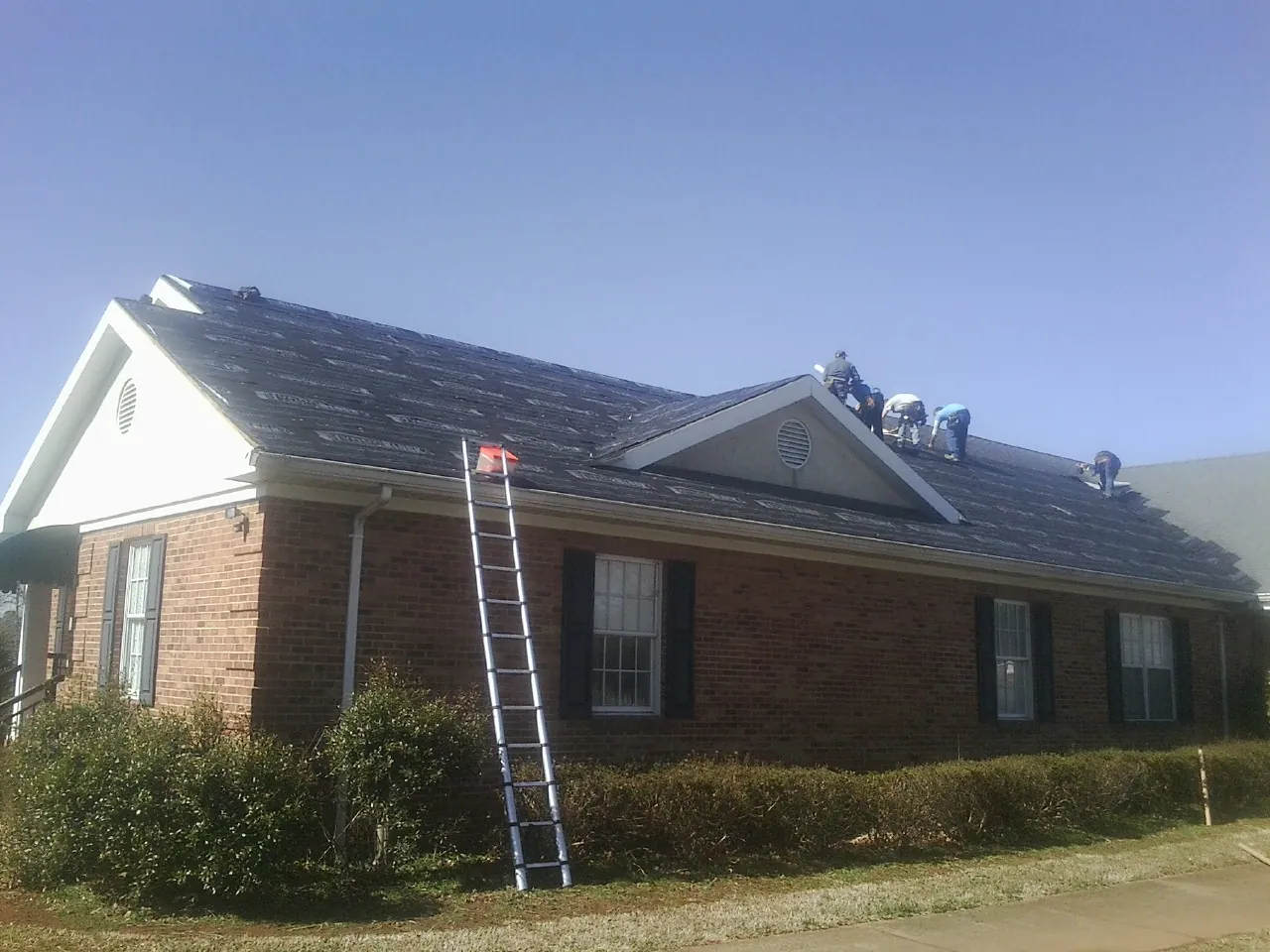 Crew tearing shingles off a brick ranch roof with a ladder set — Metal Roof Repair work by our crew in Monrovia