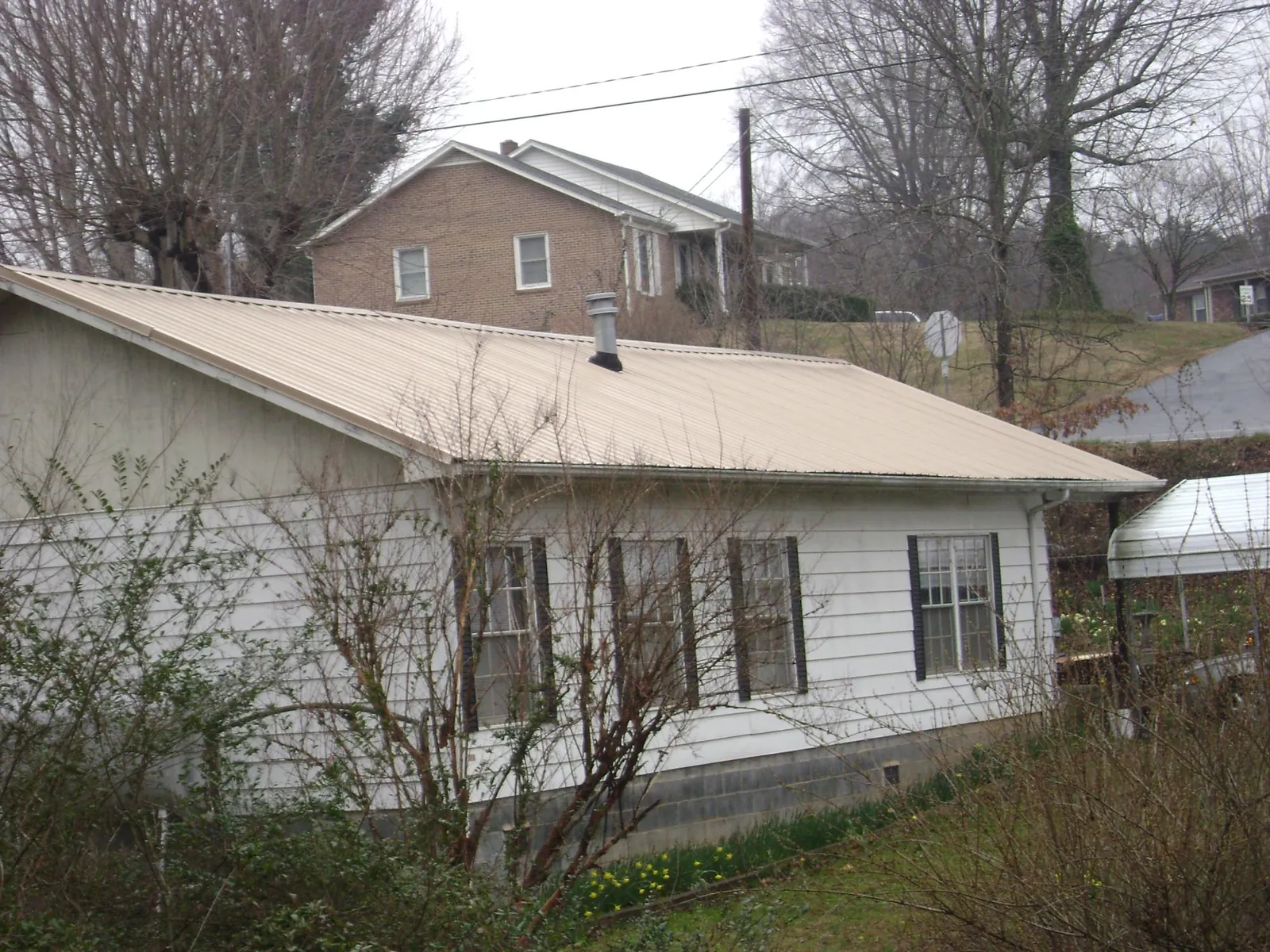Tan metal roof on a white sided house set into a hillside — Commercial Roofing by Roofing Brothers in Monrovia